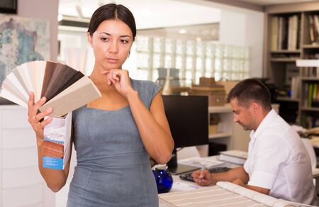 Thoughtful young woman looking for stylish materials for home furniture in storeの写真素材