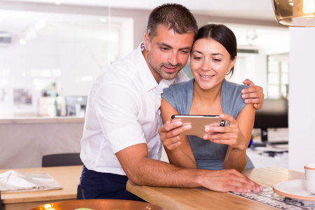 Loving couple spending time together, watching media in smartphone in comfortable kitchen