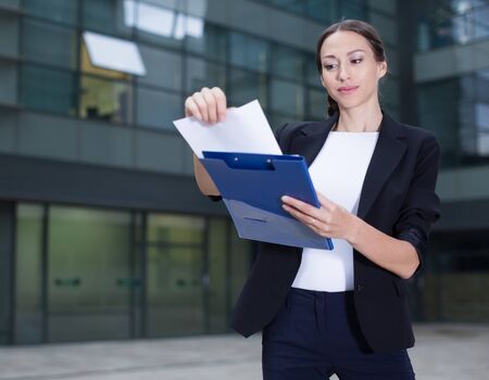 Female creative director is examining documents before signing outdoors.の写真素材