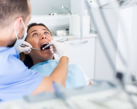 male Dentist is treating patient which is sitting in dental chair in clinicの写真素材
