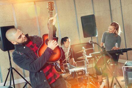 Bearded guy soloist playing the guitar and singing with two girls of his music band at studioの写真素材