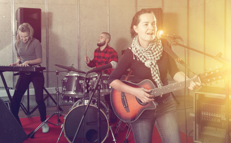Rehearsal of music band. Beautiful female guitar player and singer practicing with band members in...