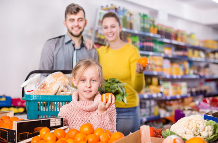 Happy little girl with loving parents choosing sweet mandarins in supermarketの写真素材
