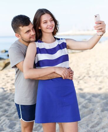 Happy loving couple resting and taking selfie on the beachの写真素材