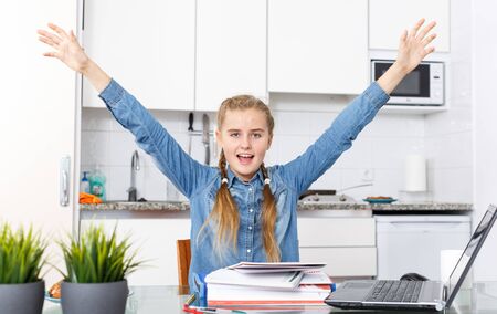 Happy teenage girl sitting at kitchen table among notebooks  and schoolbooksの写真素材