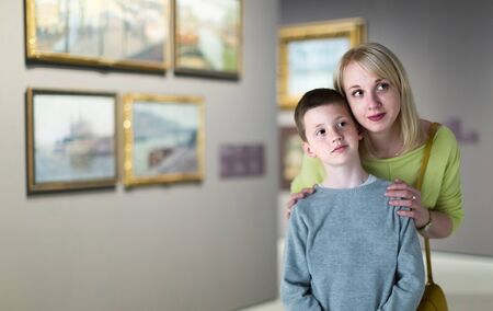 smiling mother and son looking at paintings in halls of museumの写真素材