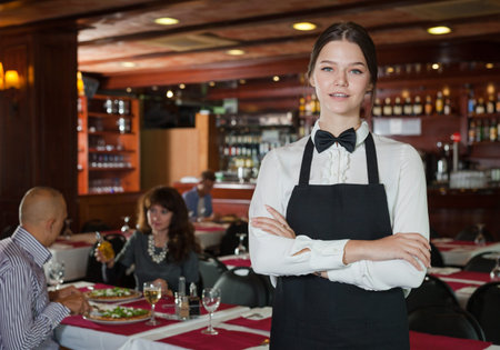 Portrait of polite waitress wearing black apron in restaurant interior