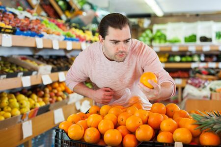 Young man customer choosing fresh oranges  on the supermarketの写真素材