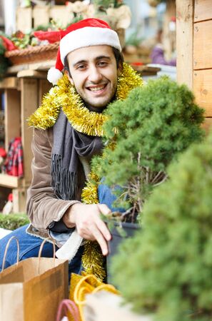 Portrait of young man choosing small Christmas tree at Christmas marketの写真素材