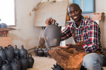 Smiling African American potter proffering clay goods he created in pottery shopの写真素材