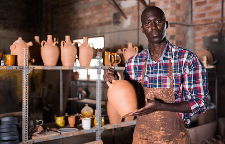 Smiling African American potter proffering clay goods he created in pottery shopの写真素材
