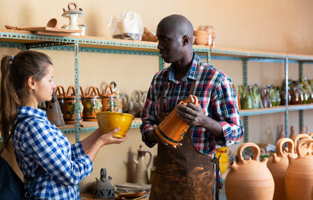 Afro male shop assistant helping girl choose ceramic production in pottery shopの写真素材