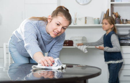 Woman with vacuum cleaner and daughter with rag