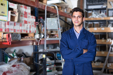 Portrait of man seller  in uniform  standing near shelving in building shop