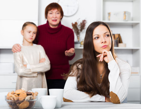 Portrait of young mother upset after quarrel with little daughter standing behind with grandma
