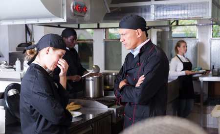 Angry male chef talking to his female assistant in commercial kitchen