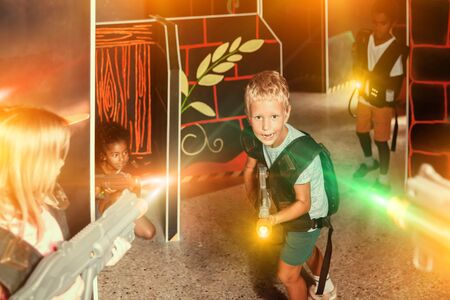 Portrait of laughing tweenager boy with laser gun having fun on dark lasertag arenaの写真素材
