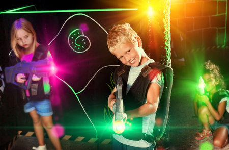Emotional preteen boy with a laser pistol playing laser tag with friends on the dark labyrinthの写真素材