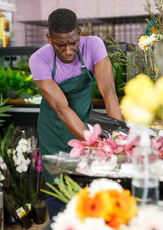 Thoughtful African-American man florist working in floral shop, sorting flowersの写真素材
