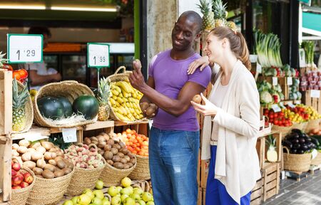 Positive couple is shopping and choosing kiwi in the fruit market outdoorsの写真素材
