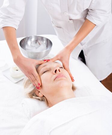 Aged smiling woman having professional face massage in spa salonの写真素材