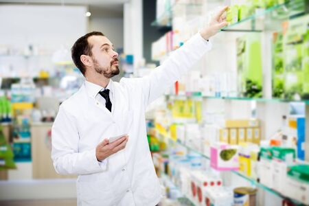 Positive man pharmacist searching for reliable drug in pharmacyの写真素材