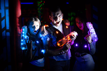 Happy young people with laser pistols posing together on dark laser tag labyrinth