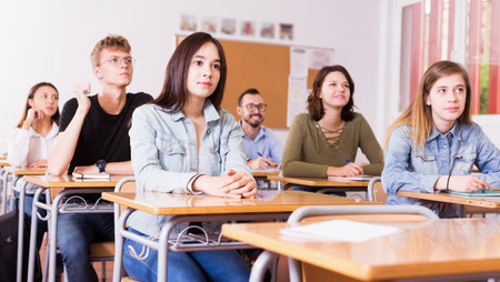 Portrait of positive young girl who is sitting at the desk in the classroom.