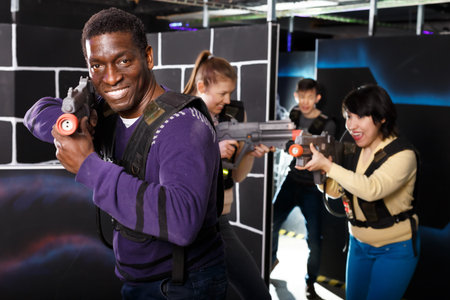 Emotional African man with a laser pistol playing laser tag with friends at a dark labyrinthの写真素材