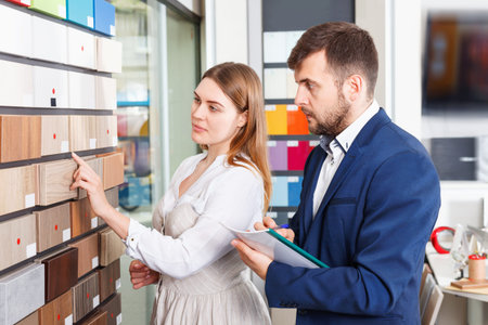 Competent diligent positive  seller in showroom helping satisfied pleasant smiling female client to choose furniture materials for her apartmentの写真素材