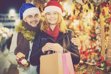 Smiling girl with boy in Christmas hat choosing decorations at marketの写真素材