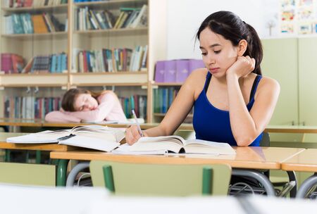 Young girl is sitting at the desk and reading text in the classroom in the school.の写真素材
