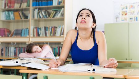 Girl is pondering about complicated task at the desk in the classroom.の写真素材