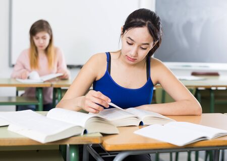 Girl is sitting at the desk and writing homework in the classroom.の写真素材