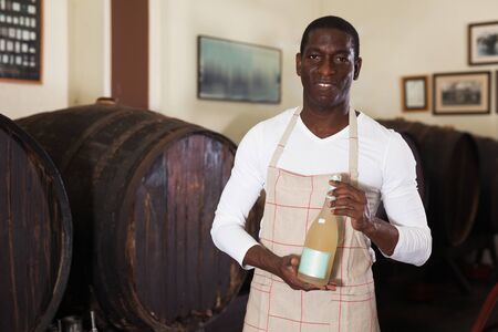 Positive male seller recommending bottle of wine for purchase in wine houseの写真素材