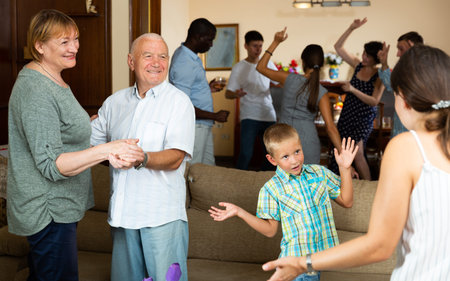 Cheerful elderly couple dancing during family holiday celebration together with their children and...
