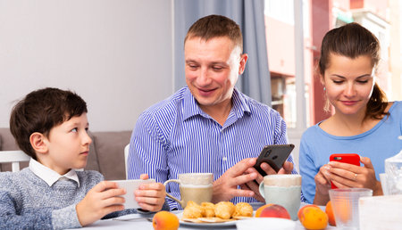 Modern young family absorbedly looking at smartphones in home interior