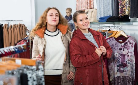 Portrait of two young attractive women posing wearing coats in clothing storeの写真素材