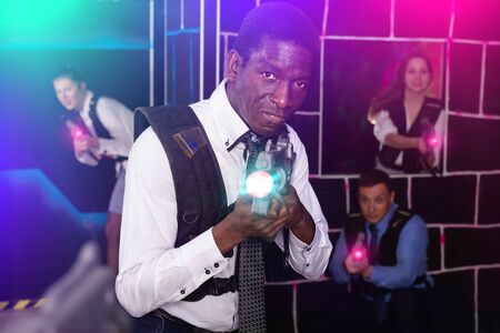 Modern Afro man and his colleagues having corporative entertainment in laser tag roomの写真素材