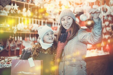 Woman and her daughter are preparing for Christmas and choosing balls on the tree outdoor.の写真素材