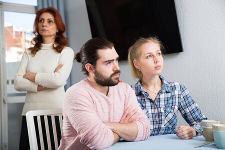 Upset mature woman talking with sad daughter and her boyfriend at home interiorの写真素材