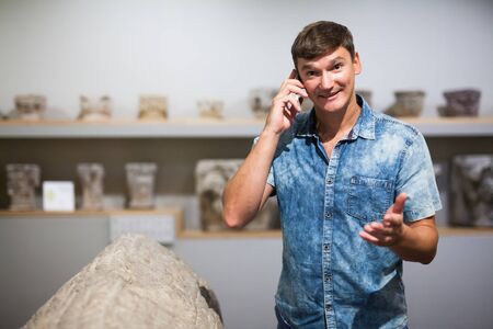 Young man talking by phone in hall of historical museumの写真素材