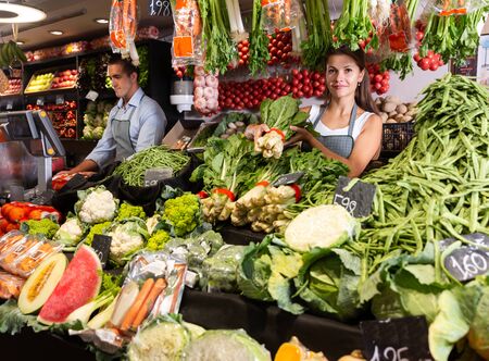 Two glad sellers working behind the counter of vegetable shopの写真素材