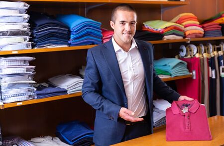 Adult salesman offering stylish woven polo shirt in men clothing storeの写真素材