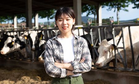 Portrait of chinese female farmer who is standing at her workplace near cows at the farm outdoorsの写真素材