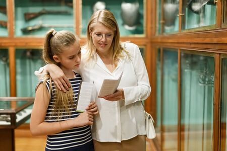 Portrait of woman with girl holding guidebook, standing in museum of artの写真素材