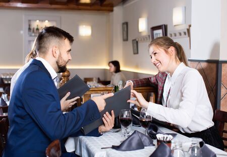 Ñheerful glad  smiling friends choosing dishes out of menu card in restaurantの写真素材