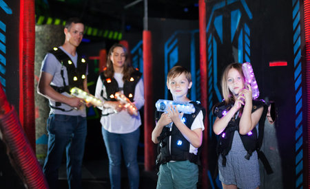 Excited kids aiming laser guns at other players during lasertag game with parents in dark roomの写真素材
