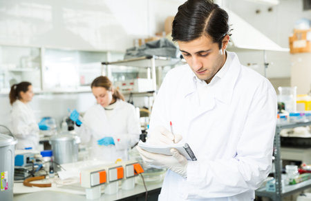 Student of Faculty of Biology performing experiments in university laboratory, writing results in...