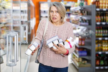 Disturbed and amazed woman reading contents of goods when shopping in food department of supermarketの写真素材